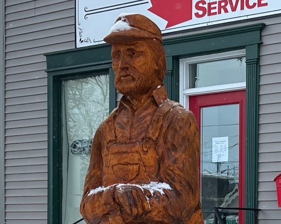 A wood carving of a farmer out front of a business in Orangeville